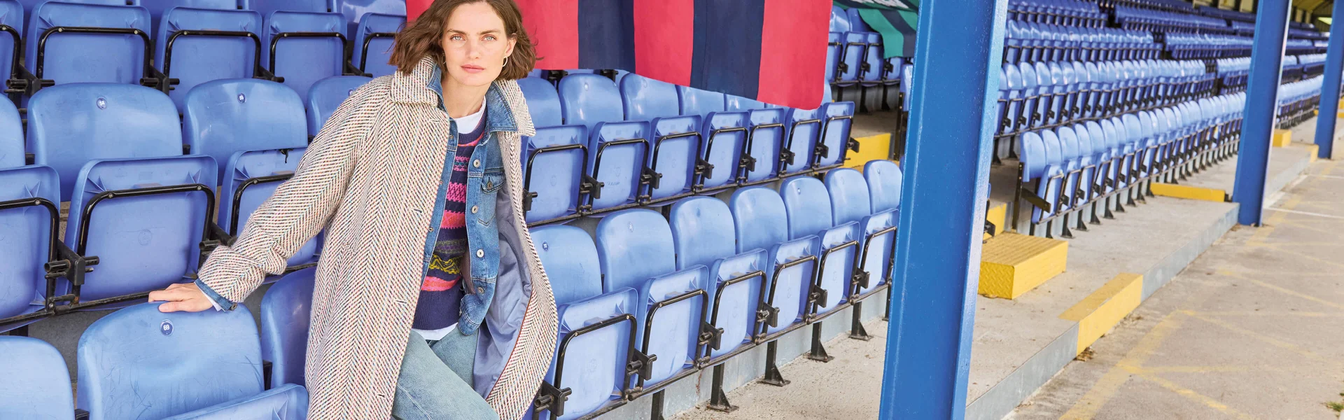 Femme appuyée sur des sièges bleus portant un long manteau beige